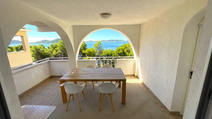 überdachte Terrasse Helle Terrasse mit Blick auf das Wasser und Bäume, ein Tisch mit Stühlen.