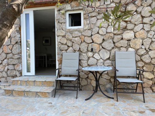Terrasse Steinmauer mit zwei Gartenstühlen und einem kleinen Tisch im Freien.