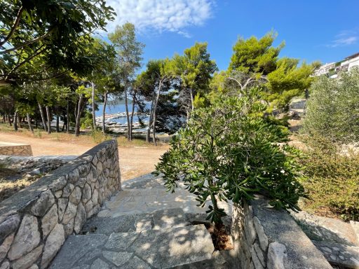Zugang zum Meer Blick auf einen Gartenweg mit Bäumen und Blick auf das Wasser im Hintergrund.