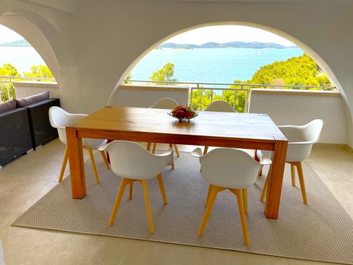Essbereich draußen Moderner Essbereich mit Holztisch und weißen Stühlen, Blick auf das Wasser und Bäume.