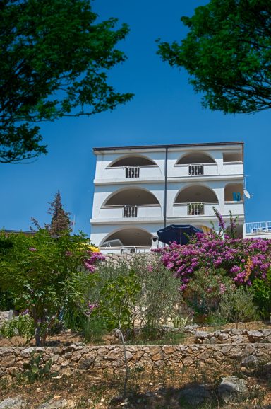 Haus Ansicht Drei stöckiges Haus mit Balkon, umgeben von bunten Blumen und Grünpflanzen.